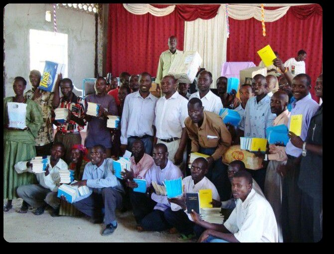 Community members holding newly distributed Turkana literacy books at a TLDB literacy day