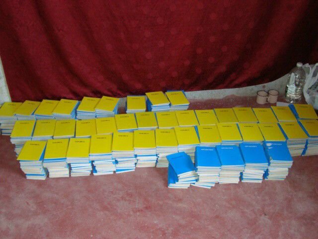 Printed Turkana literacy booklets in yellow and blue covers laid out at a TLDB production event